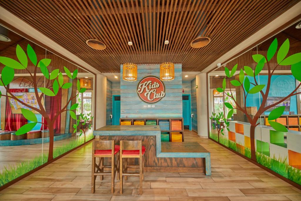 Krāsains bērnu klubs ar koka mēbelēm un dzīvīgu dekoru, kurā ir zaļi koki un zālājs. Interjers ir draudzīgs un aicinošs bērniem.
