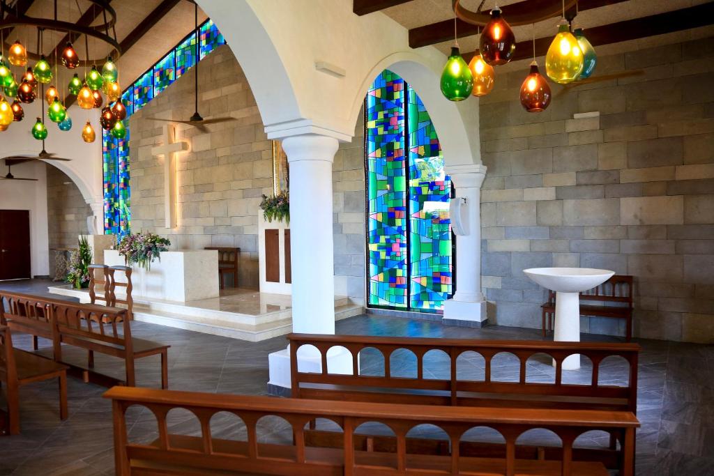 Mūsdienīga baznīca ar krāsainu stikla logu, koka soliem un gaismas ķermeņiem. Interjers apvieno eleganci un vienkāršību, radot mierīgu atmosfēru.