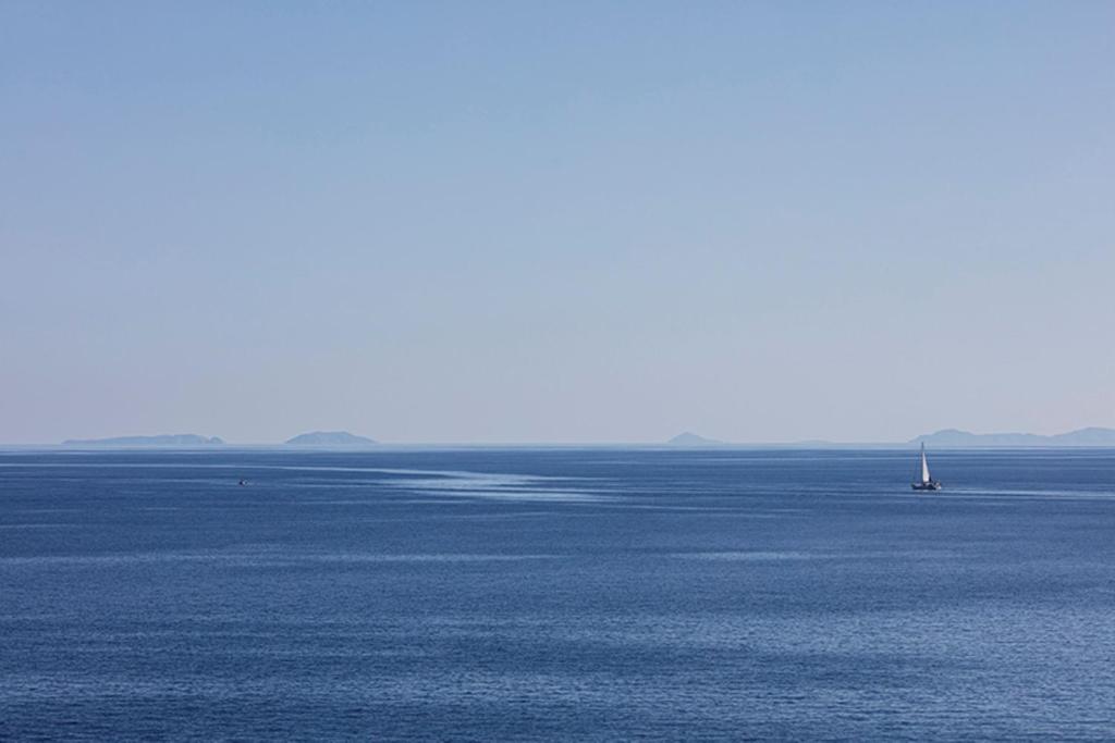 Mierīga jūras ainava ar vienu laivu un attālinātām salām horizontā. Zilā debess un ūdens harmonija rada relaksējošu atmosfēru.