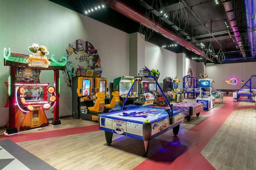 Spēļu zāle ar dažādām arcade spēlēm, tostarp gaisa hokeju un izklaidējošām automātiem. Apgaismojums un mūsdienīga dizaina elementi rada jautru atmosfēru.