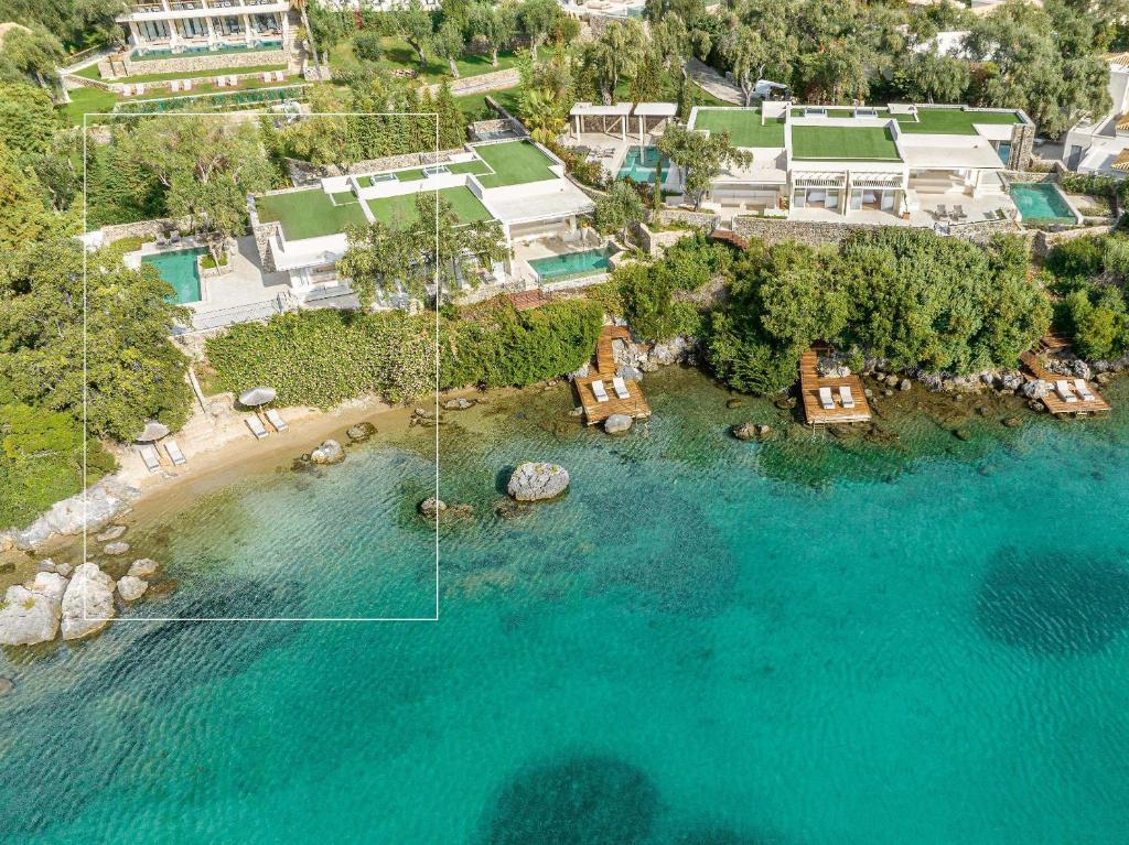 Pārskatāms skats uz luksus villas kompleksu blakus krastam ar tīru, zilu ūdeni un sauļošanās platformām.