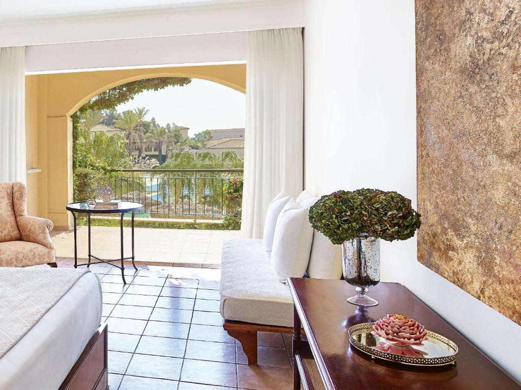 Mūsdienīgs viesnīcas numurs ar skatu uz dārzu, kurā redzami tropiski augi un baseins. Interjerā ir ērti mēbeļu komplekti un eleganti dekoratīvi elementi.