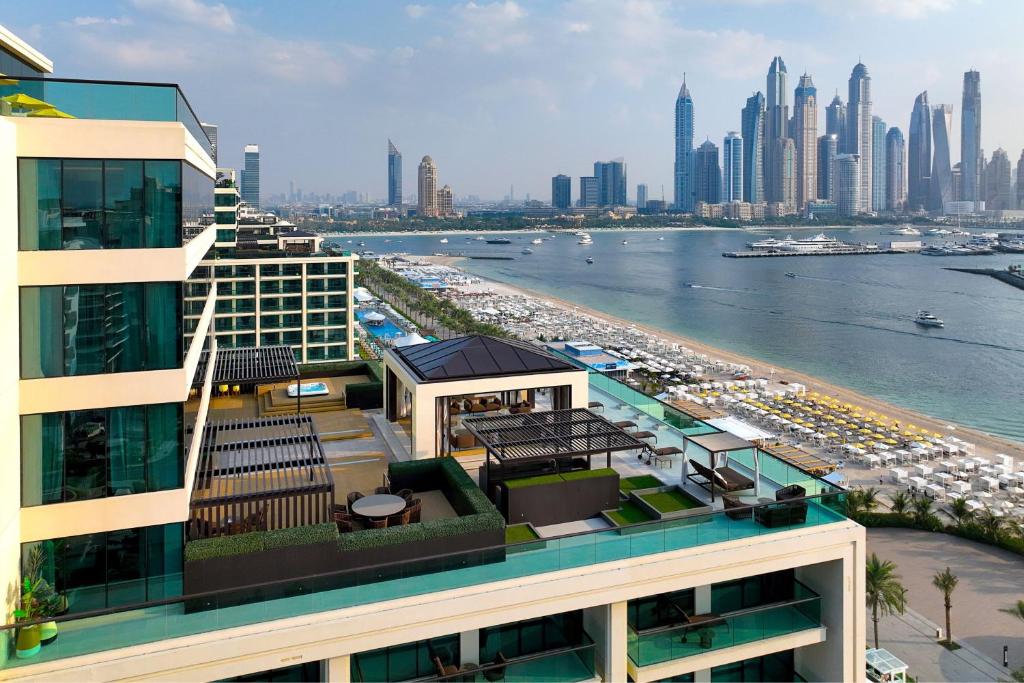 Mūsdienīgs viesnīcas skats ar ainavisku pludmali un Dubaijas debesskrāpjiem fonā, piedāvājot elegantu arhitektūru un relaksējošas atpūtas vietas.