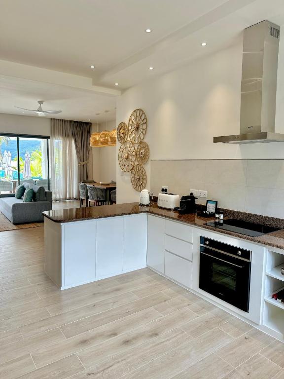 Mūsdienīga virtuve ar granīta virsmu, iestrādātu plīti un skatu uz dzīvojamo istabu, kurā ir ērta dīvāna zona. Interjers ir gaišs un elegants, ar dekoratīvām sienu rotāšanām un logu, kas ved uz āra terasi.