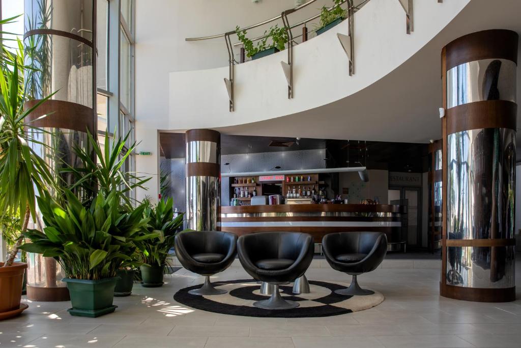 Mūsdienīgs viesnīcas reģistratūras interjers ar melnām krēslām, dekoratīvām augu kompozīcijām un elegantu bāra letes dizainu.
