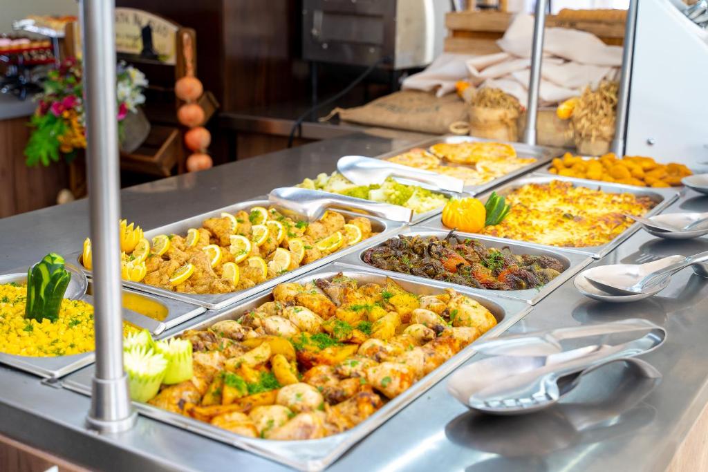 Dažādu ēdienu bufete ar krāsainiem dārzeņiem, gaļas ēdieniem un garnējumiem, izkārtota uz sudraba galda.