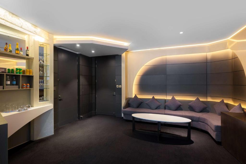 Mūsdienīgs atpūtas istabas interjers ar pelēku dīvānu un apgaismojumu. Uz plaukta redzami dzērieni un glāzes, radot elegantu atmosfēru.