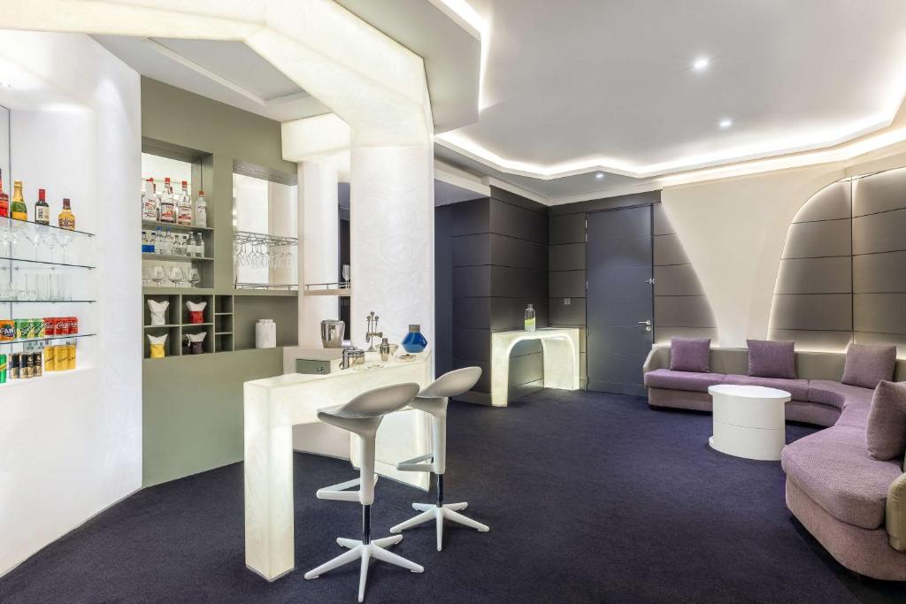 Moderns interjers ar elegantu bāru un relaksējošām atpūtas zonām, apgaismots ar mūsdienīgu apgaismojumu. Barā redzami dzērieni un glāzes, radot viesmīlīgu atmosfēru.