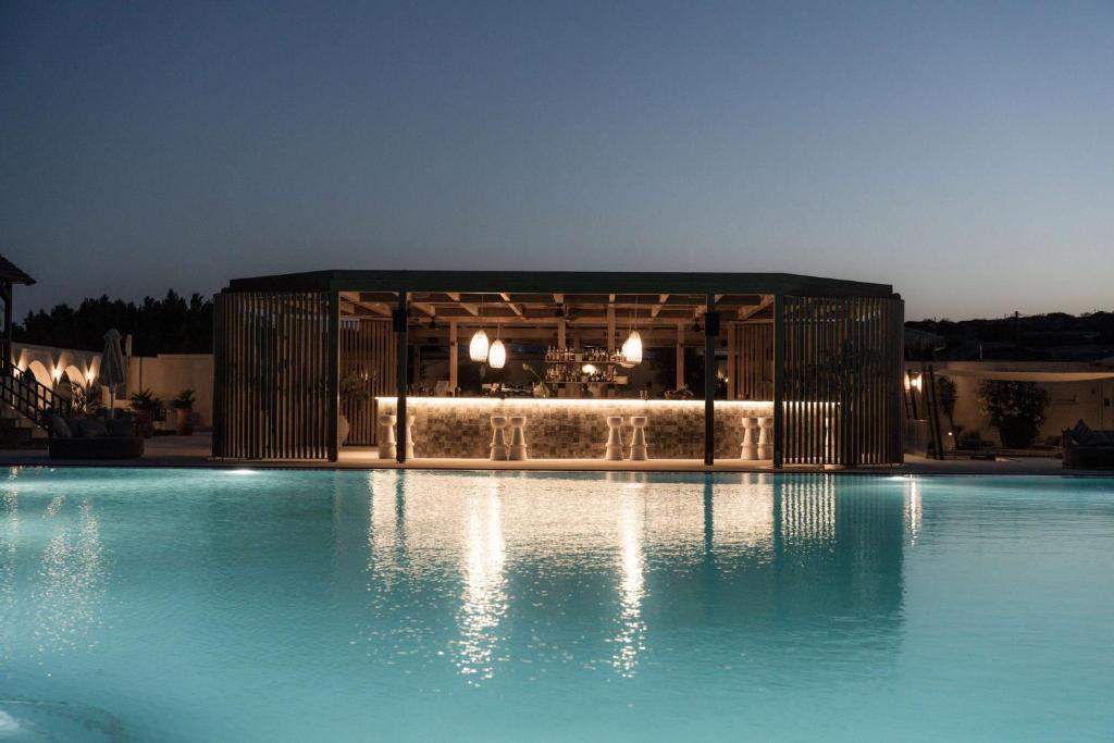 Mūsdienīgs bārs pie baseina vakara apgaismojumā, ar apgaismojumu un stilīgu arhitektūru. Ūdens virsma spīd un atspoguļo apkārtējo vidi.