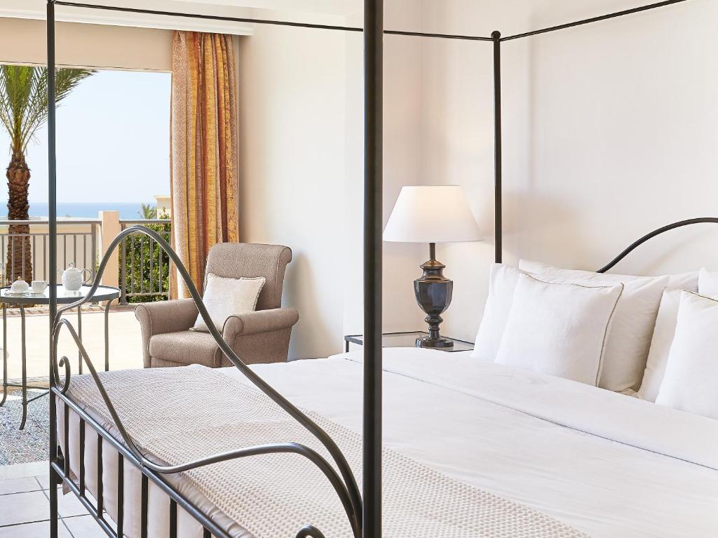 Eleganta viesnīcas numura interjers ar četrām stūriem, kurā redzams ērts gultas rāmītis, mīksta krēsla stūris un skats uz jūru caur logu. Ideāla vieta relaksācijai un atpūtai.