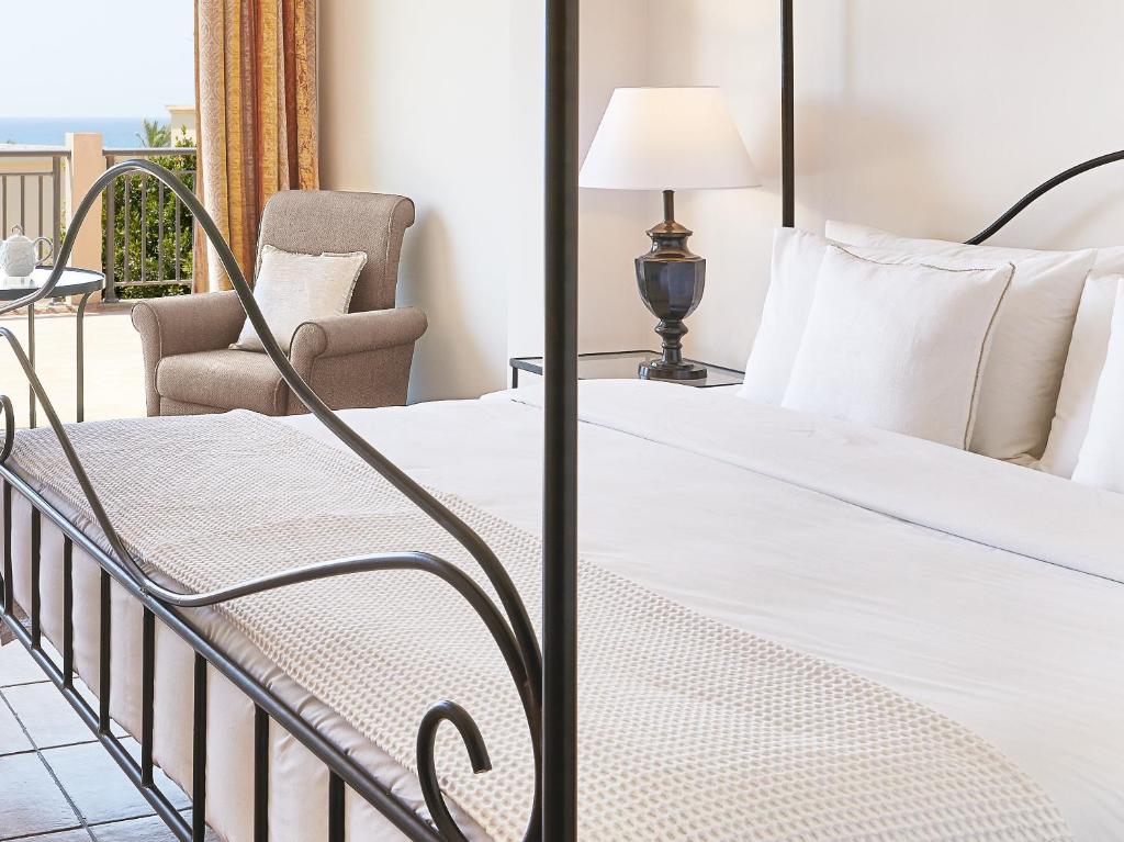 Mūsdienīga guļamistaba ar gultu un ērtu krēslu, kas nodrošina skatu uz jūru. Telpā ir arī lampiņa un dabiska gaisma, radot mierīgu atmosfēru.