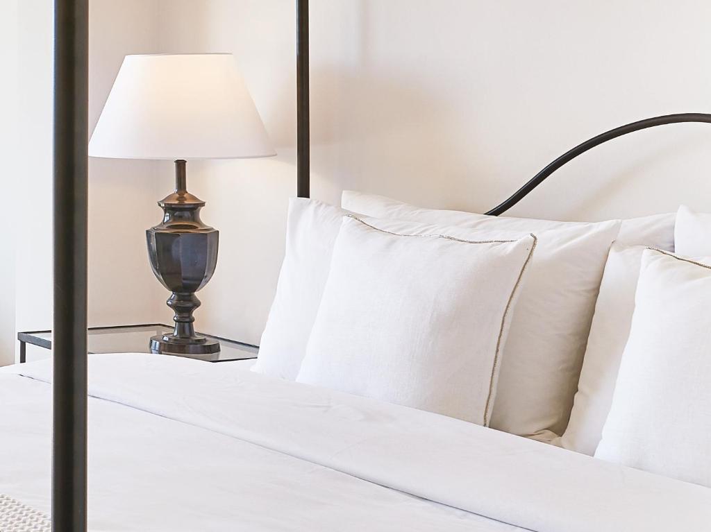 Mūsdienīgi iekārtots guļamistabas stūris ar gultu, baltām spilveniem un elegantu galda lampu.