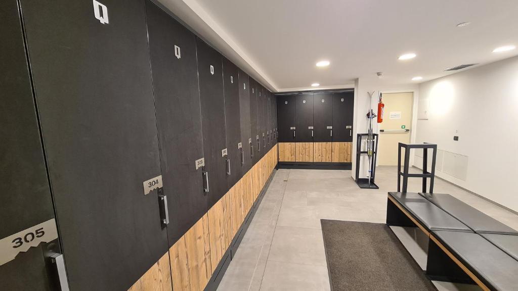 Apsildāmā telpa ar melnām skapīšiem un koka apakšdaļu, kas izskatās moderni un eleganti. Skapīšu numuri ir redzami, un telpā ir arī sēžamā vieta.