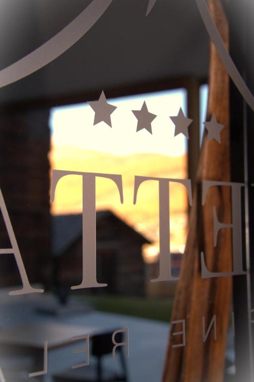 Logotips ar četriem zvaigznēm, kas atspoguļojas stiklā, ar ainavu fonā.