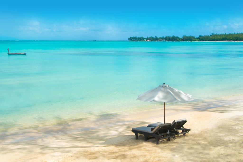 Pludmales ainava ar divām sauļošanās krēslām un saules vairogu, fons ar tīru zilo ūdeni un debesīm.