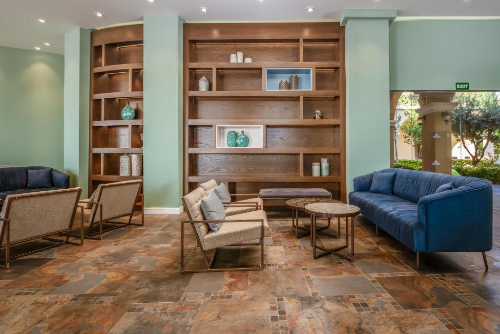 Mūsdienīgs viesnīcas interjers ar elegantiem mēbeļu komplektiem, koka plauktiem un zaļām detaļām, radot mājīgu atmosfēru.