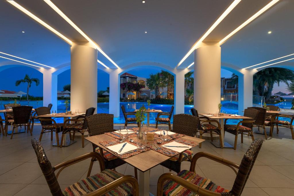 Mūsdienīgs restorāns ar elegantu interjeru un skatu uz baseinu, apgaismots ar maigu gaismu vakara stundās. Galdi ir noformēti ar galda piederumiem un dekoratīvām detaļām.