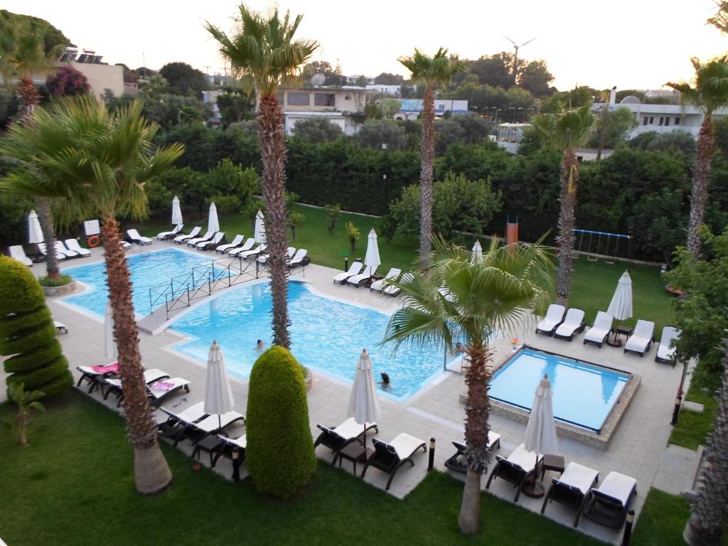 Peldbaseins ar palmām un saulessargiem, apkārt zaļā zāliena platība, lieliska vieta atpūtai un relaksācijai.