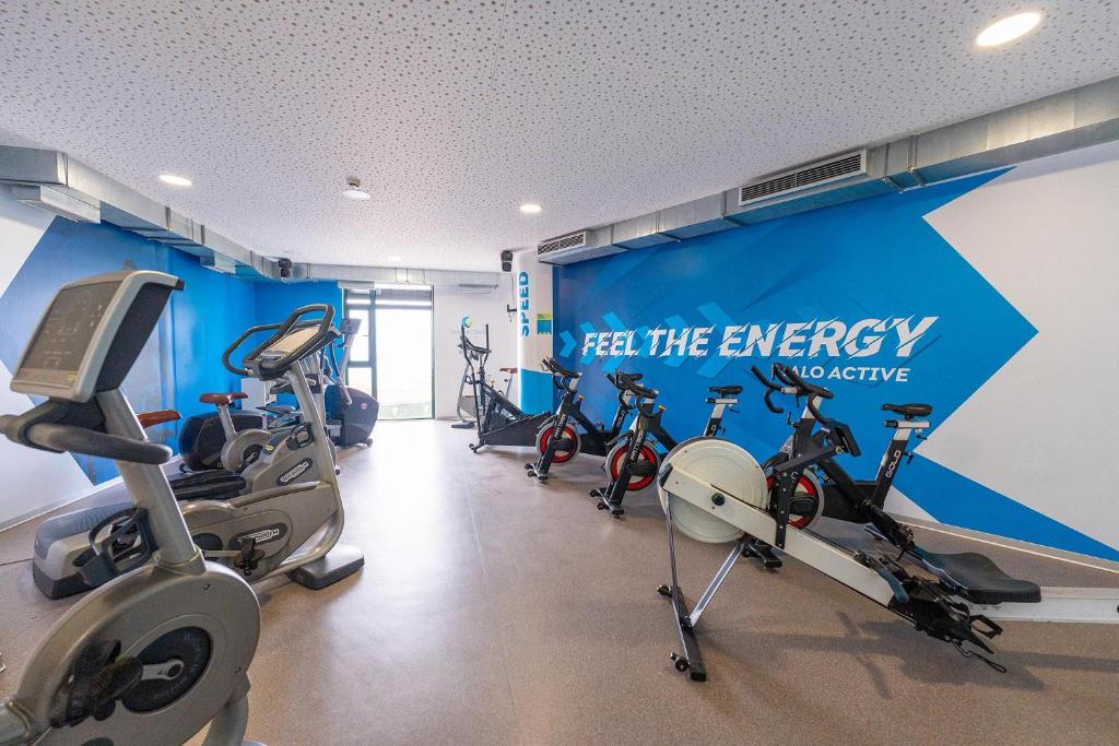 Mūsdienīgs sporta zāles interjers ar dažādiem trenažieriem un motivējošu sienas dizainu 