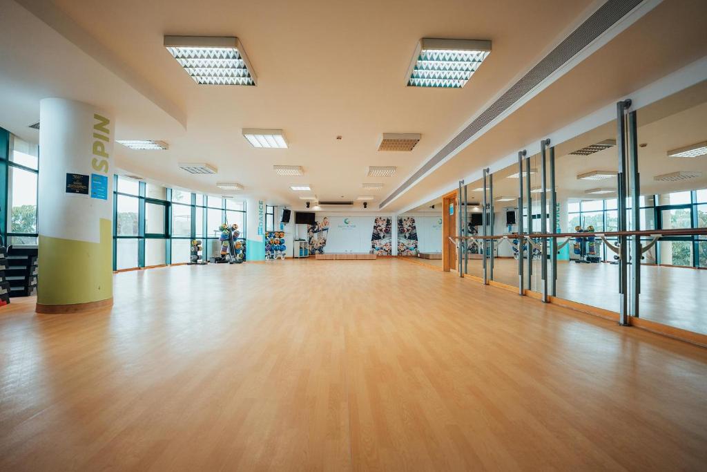 Liela, gaiša fitnesa zāle ar koka grīdu un spoguļiem. Telpa ir aprīkota ar dažādām fitness iekārtām un lieliem logiem, kas nodrošina dabisko apgaismojumu.