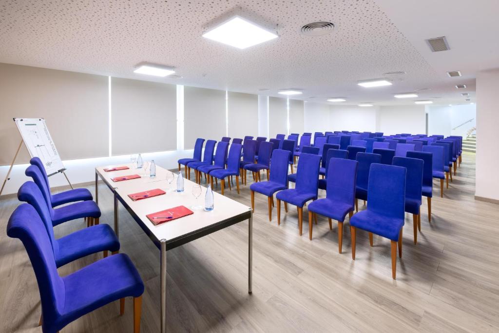Konferenču telpa ar ziliem krēsliem un galdu, sagatavota sanāksmei. Telpā ir daudz gaismas un balta krāsa dominē pārējā interjerā.
