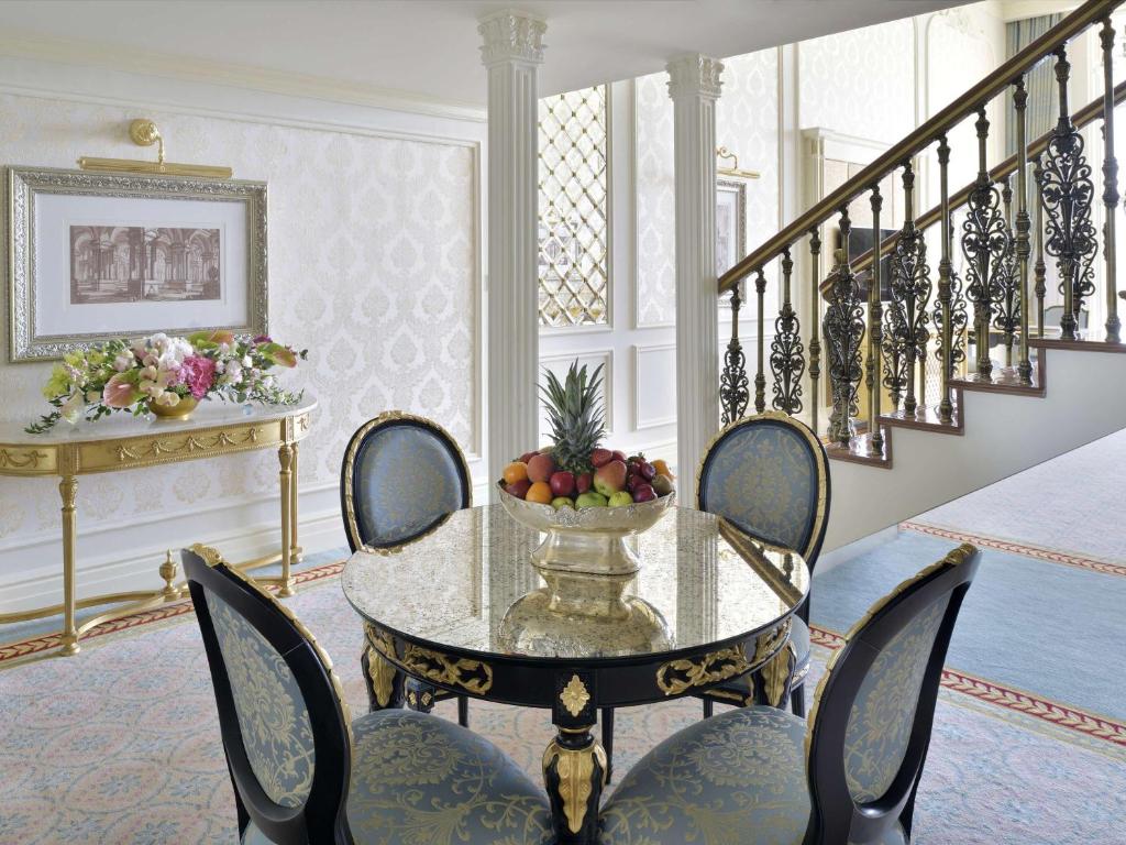 Elegants viesistabas interjers ar greznu galdu, krēslām un augļu kompozīciju. Sienas rotā izsmalcināti dekori un gleznas, radot mājīgu atmosfēru.