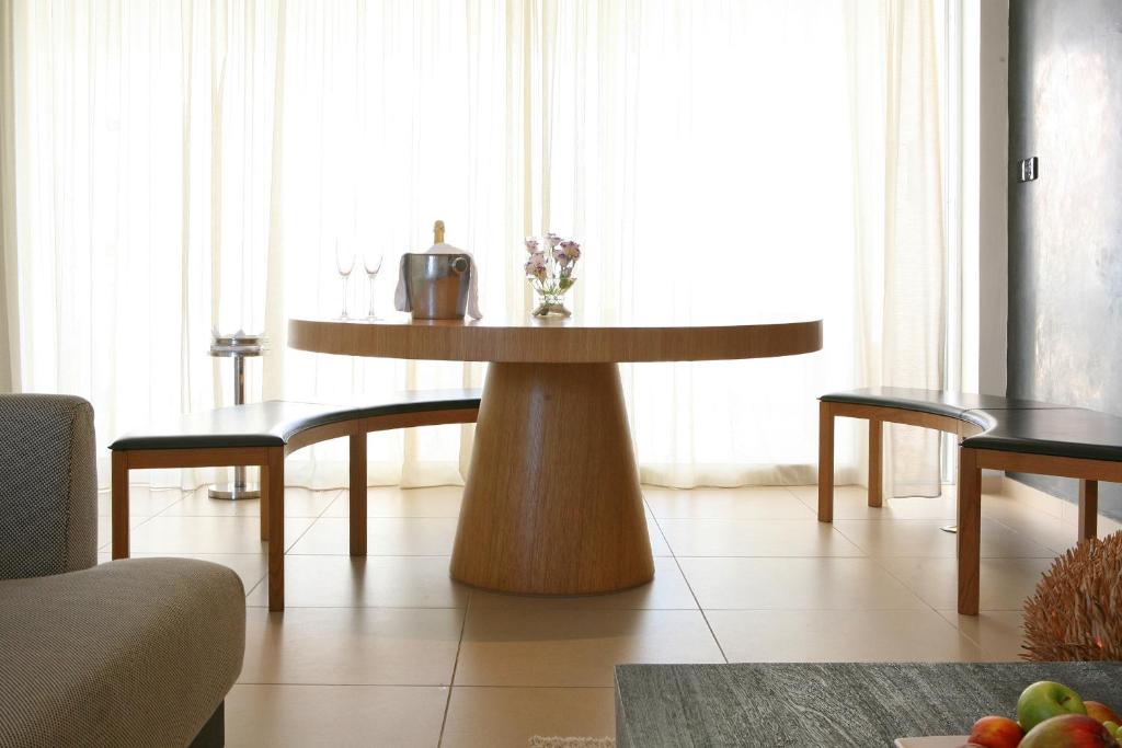 Moderns pusdienu galds ar koka kājām un melnām mīkstajām malām, apvienots ar elegantu interjeru un dabiskiem gaismas toņiem. Svaigi ziedi un dzirkstošie glāzes papildina telpas estētiku.