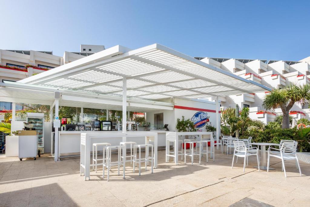 Balta un moderna baseina bārs ar ērtu sēdvietu laukumu un tropiskiem augiem apkārt, ideāls atpūtai. Saulains laiks un skaidrs debesis papildina relaksējošo atmosfēru.