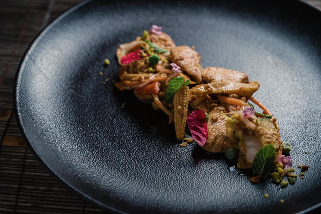 Gards un estētisks ēdiens uz melnas plāksnes, dekorēts ar ziedlapām un zaļumiem. Izcila kulinārija ar krāsainām sastāvdaļām.