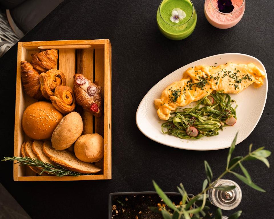 Svaigmaizītes un omlete ar dārzeņiem, pasniegtas uz melna galda, papildinātas ar dzērieniem un dekoratīvām augu detaļām.