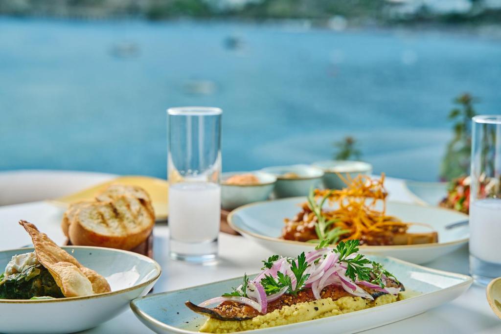 Garšīgi pasniegts ēdiens ar ceptu zivtiņu un garnējumu, fons ar ūdens ainavu un saulainu laiku. Ideāla vieta maltītei pie jūras.