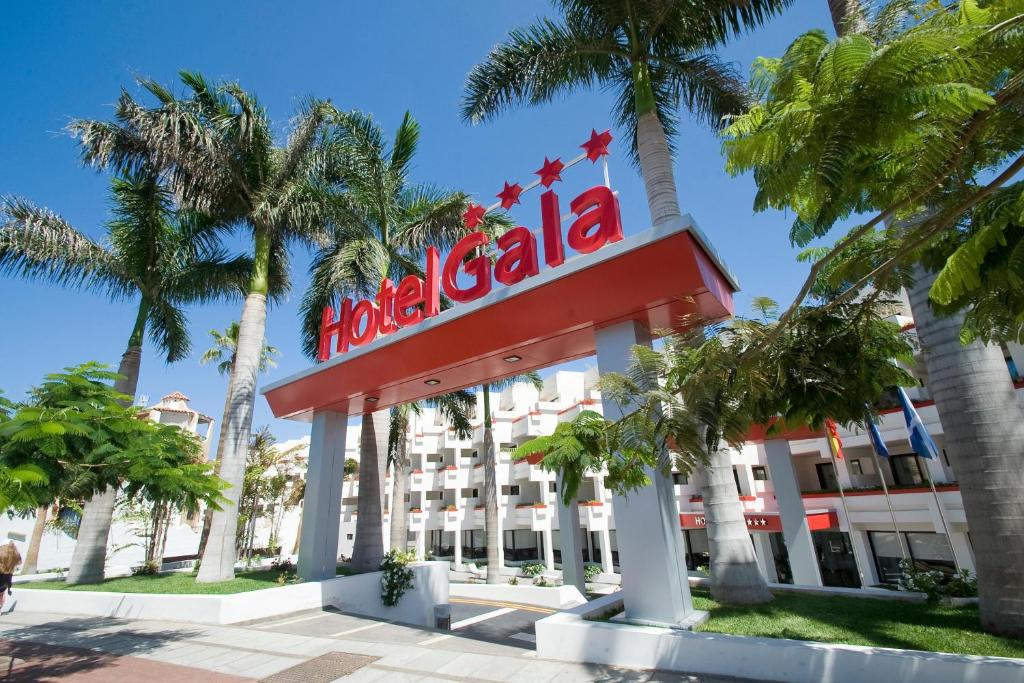 Viesnīcas "Hotel Gala" ieeja ar palmām un skaidru zilo debesu fonu, izceļot tās modernu arhitektūru un viesmīlīgu atmosfēru.
