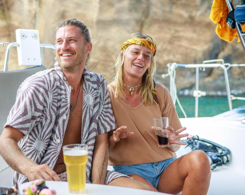 Divi jaunieši sēž uz jahtas, priecīgi sarunājoties un baudot dzērienus. Viņi ir brīvā stila apģērbā, un fons ir skaista jūra un klints.