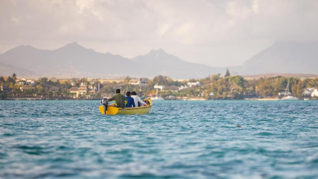 Dzeltena laiva ar cilvēkiem, kas dodas jūrā, fons ar kalniem un piekrastes ainavu.