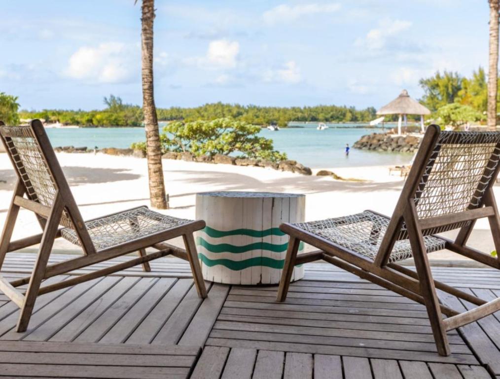 Koka krēsli ar skatu uz pludmali un jūru, kur redzamas palmas un laivas. Ideāla vieta atpūtai un relaksācijai.