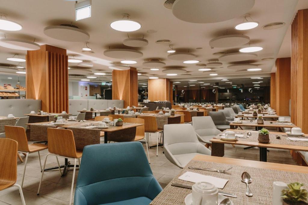 Mūsdienīgs restorāns ar elegantu interjeru un gaišām krāsām, kurā ir sakārtoti galdi ar galda piederumiem un maziem augu dekorējumiem. Atmosfēra ir brīva un aicinoša, ideāla brokastīm.