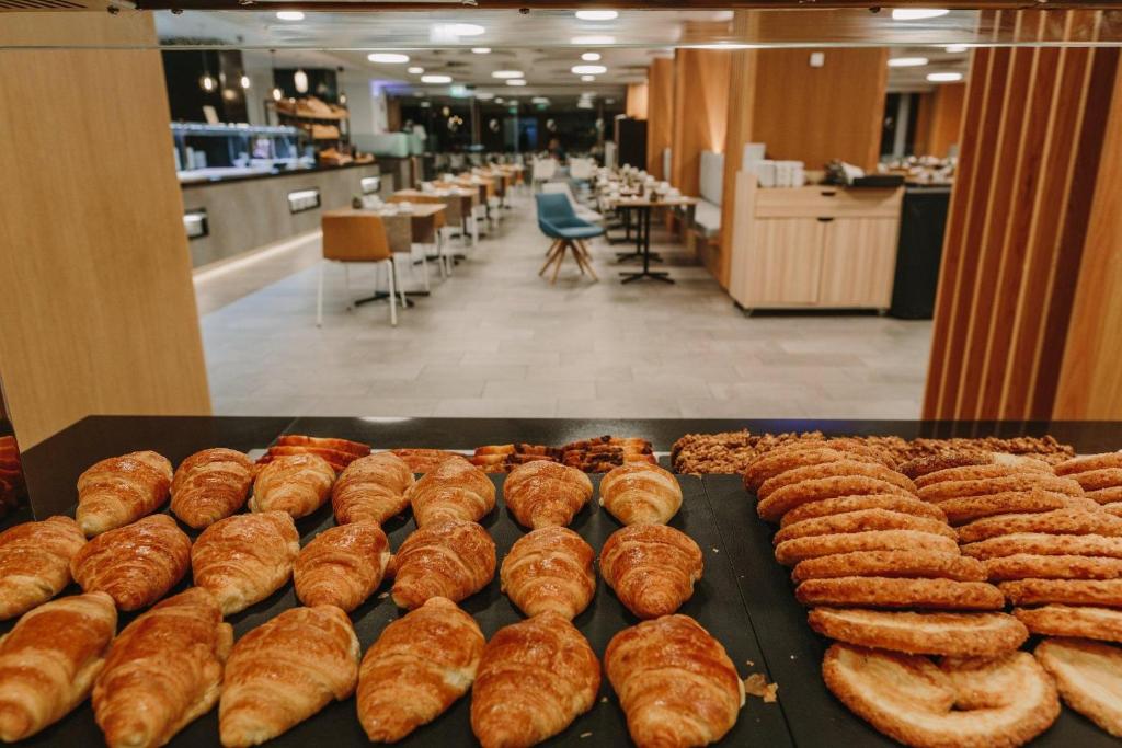 Brokastu bufete ar svaigiem kruasāniem un cepumiem, kas izkārtoti uz galda, bet fonā redzama moderna ēdamzāle ar mēbelēm.