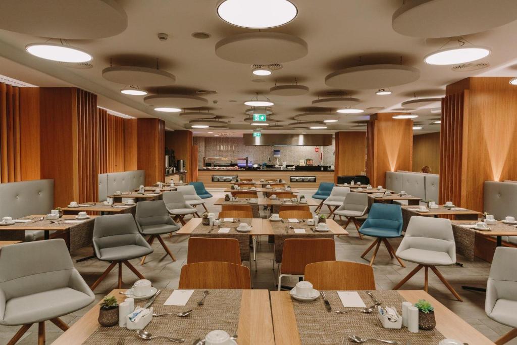 Mūsdienīgs restorāns ar elegantu interjeru, kurā ir koka akcenti un komfortablas sēdvietas. Galdi ir sakārtoti ar galda piederumiem un kafijas tases, radot viesmīlīgu atmosfēru.