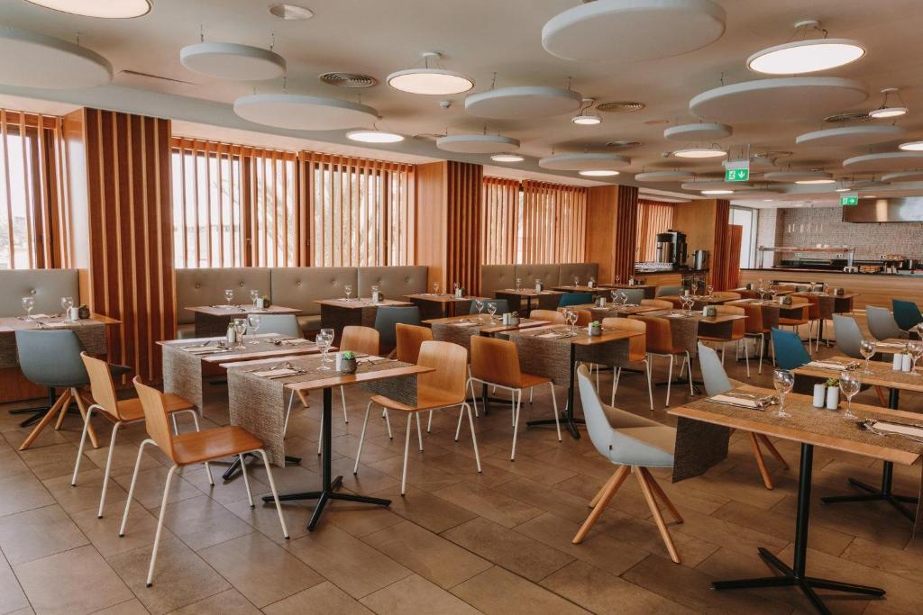 Mūsdienīga restorāna iekārtojums ar koka un pelēko toņu elementiem, apgaismojumu un eleganti klātiem galdiem. Ideāla vide relaksējošai maltītei.