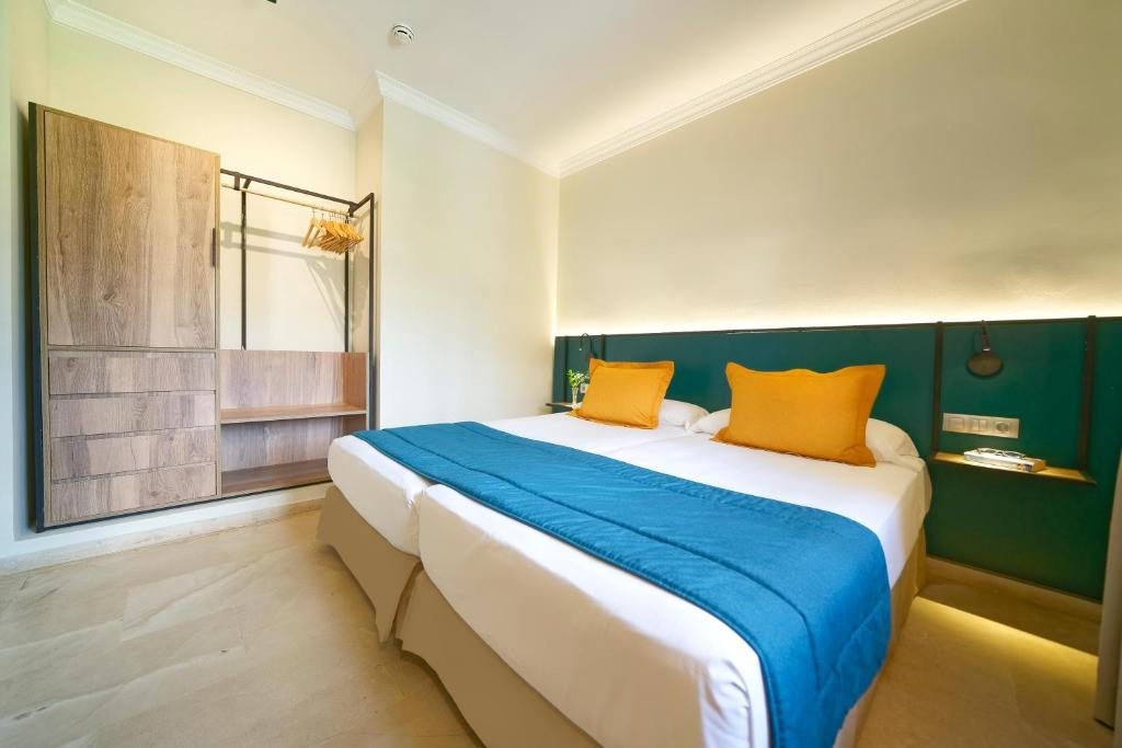 Mūsdienīgs viesnīcas numurs ar divām gultām, oranžām spilveniem un koka skapīti. Interjers ir gaišs un elegants, ar zilo gultas pārklāju un minimālistisku apgaismojumu.