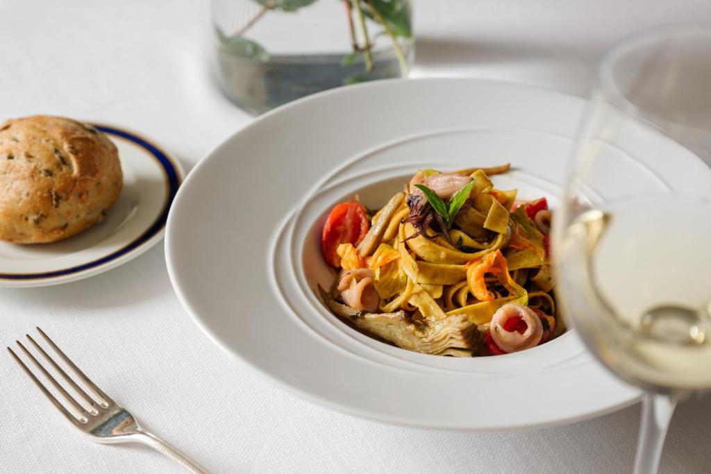 Garšīgas makaronu porcijas ar dārzeņiem un garnelēm, pasniegtas ar baltvīnu un maizi. Eleganta restorāna iestatījums.