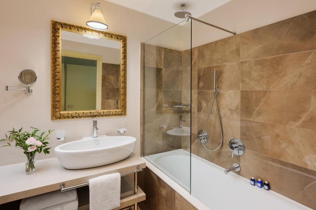 Mūsdienīgs vannas istabas iekārtojums ar elegantu spoguli, dušas kabīni un vannu. Interjers ir veidots ar siltu krāsu paleti un dekoratīvām detaļām, radot patīkamu atmosfēru.