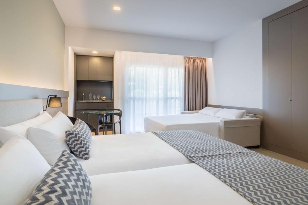 Mūsdienīgs viesnīcas numurs ar divām gultām, ērtu dīvānu un nelielu darba zonu. Telpā ir lieli logi, kas nodrošina dabīgu apgaismojumu.