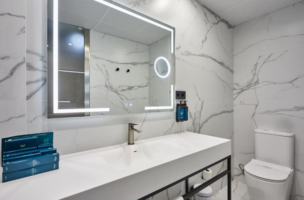 Mūsdienīgs vannas istabas interjers ar marmora izskatu, elegantu spoguli ar apgaismojumu un minimālistisku izlietni.