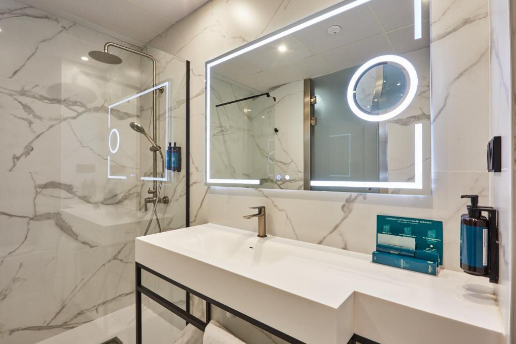 Mūsdienīga vannas istaba ar marmora sienām, apgaismotu spoguli un elegantu izlietni. Tīrās līnijas un minimālistisks dizains rada stilīgu atmosfēru.