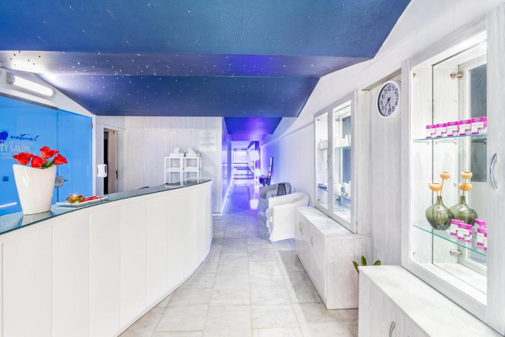 Mūsdienīgs skaistumkopšanas salons ar gaišu interjeru un elegantu pieņemšanas zonu, kas iekārtota ar stikla vitrīnām un ziediem. Telpā ir redzama relaksējoša atmosfēra ar siltu apgaismojumu.
