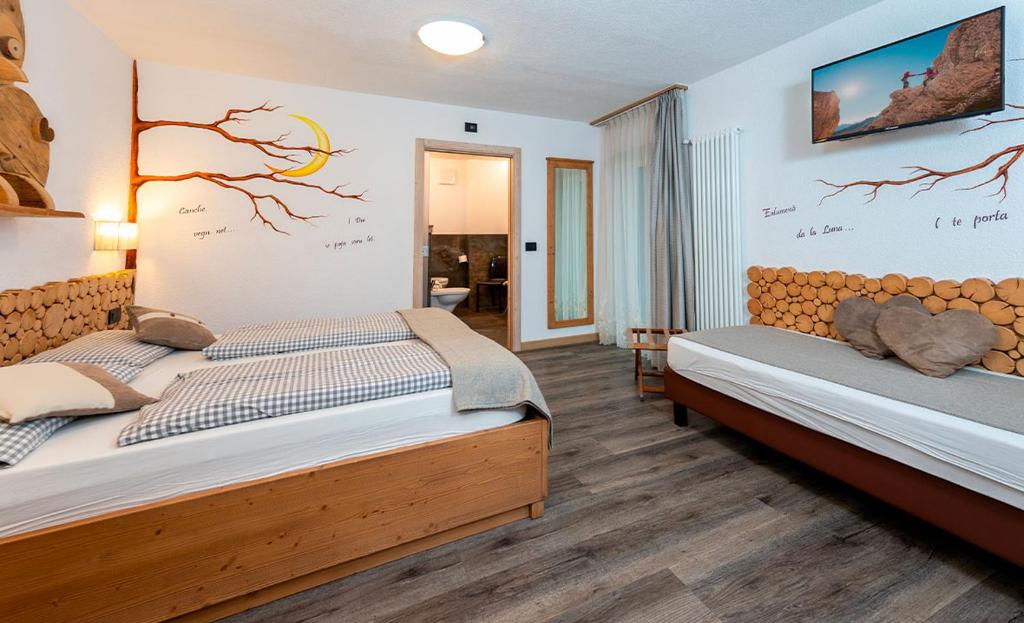 Mūsdienīgs guļamistabas interjers ar diviem gultām, koka akcentiem un sienu dekoru, kas ietver koka zaru un mēness attēlus. Telpā ir televizors un komfortabla atpūtas zona.