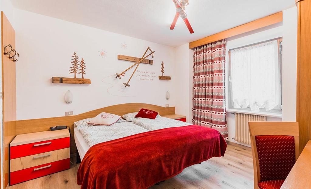 Mūsdienīga guļamistaba ar sarkanu gultas pārklāju, koka mēbelēm un dekoratīviem elementiem, piemēram, koka plauktiem un aizkariem ar sirsniņām. Interjers rada mājīgu un siltu atmosfēru.