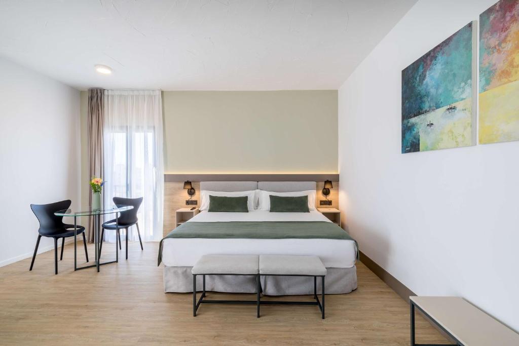 Mūsdienīga viesnīcas numura interjers ar divguļamo gultu, galdiņu un krēsliem, kā arī divām gleznām uz sienas. Gaisma un telpas platums rada komfortablu atmosfēru.