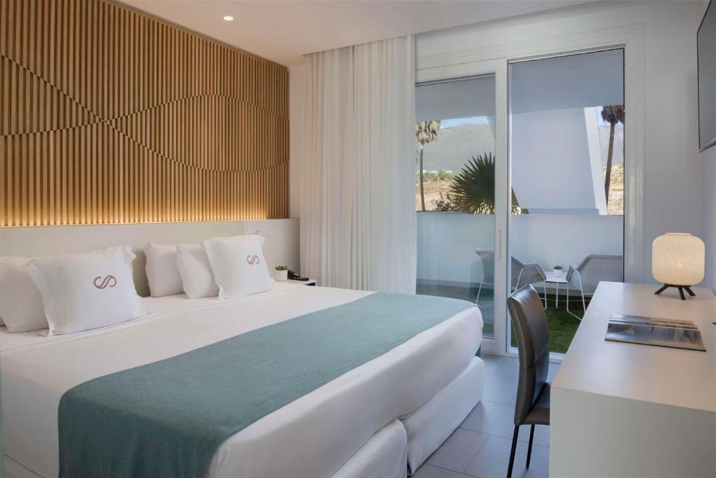 Mūsdienīga viesnīcas istaba ar elegantu koka apdari, plašu gultu un balkonu ar skatu uz dabu. Istabā ir gaišas krāsas un moderna mēbeles, radot relaksējošu atmosfēru.